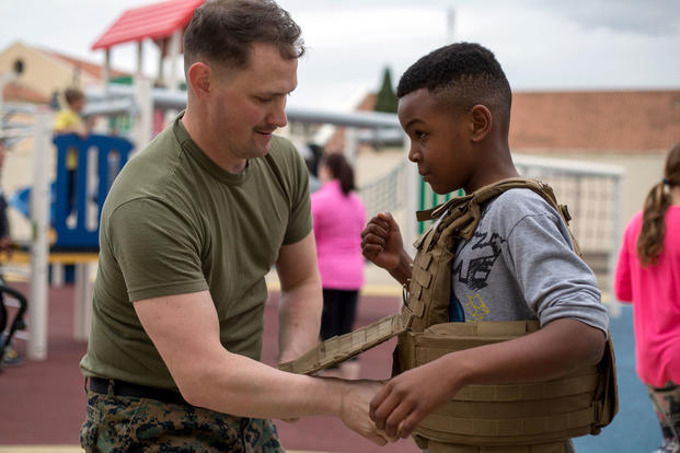A U.S. Marine assigned to Special Purpose Marine Air-Ground Task Force-Crisis Response Africa helps a child into a protective vest during a gear demonstration. (U.S. Marine Corps/Taylor W. Cooper)