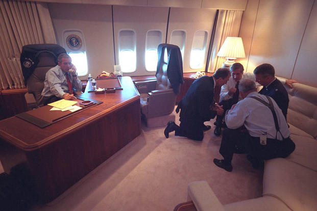 President George W. Bush talks on the telephone Sept. 11, 2001, as senior staff huddle aboard Air Force One. (Photo by Eric Draper, Courtesy of the George W. Bush Presidential Library) 