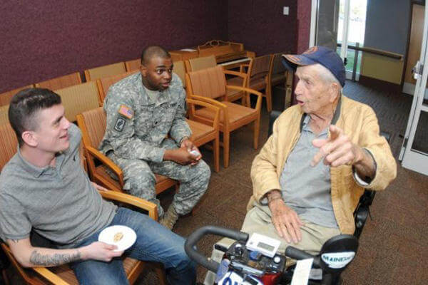 Older veteran in a wheelchair talking with service members.