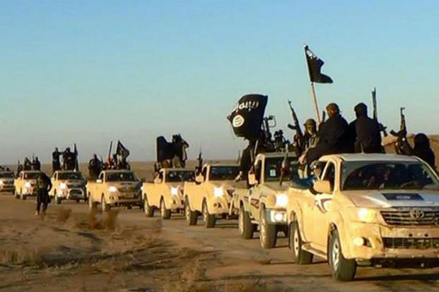 In this undated file photo released by a militant website, which has been verified and is consistent with other AP reporting, militants of the Islamic State group hold up their weapons and wave its flags in a convoy. (Militant website via AP, file)