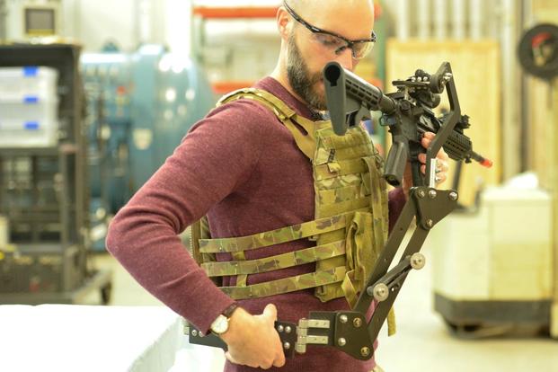 Army Research Lab engineer Dan Baechle demonstrates how to strap on a mechanical arm designed to reduce soldier fatigue and improve weapon’s accuracy. (Photo: U.S. Army)