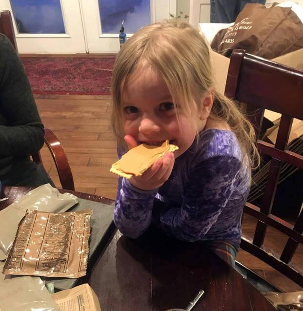 Angelina Vankirk, 6, smiles while taking a bite of a meal, ready-to-eat cracker with peanut butter during her Family’s MRE night near Fort Drum, New York. (Courtesy of Patrick Vankirk)