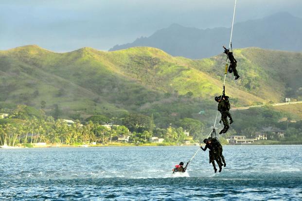Navy SEAL divers dangle from a rope attached to an Army UH-60 Black Hawk helicopter.
