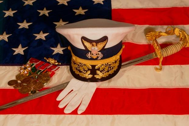 Officer's combination cover, sword, white gloves and medal rack laying upon an American flag. (U.S. Coast Guard photo)