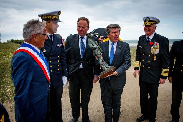 Retired Rear Adm. Frank Thorp IV holds a miniature version of the "Lone Sailor" statue during a United States Navy Memorial and Frogmen Association of Utah Beach dedication ceremony in Normandy, France, June 6, 2019. (U.S. Navy photo/Jonathan Nelson)