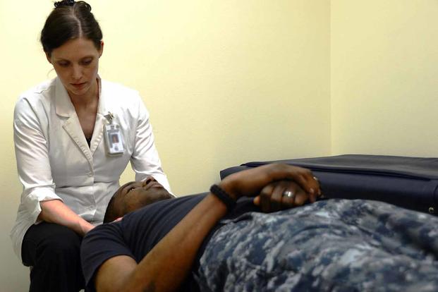 A chiropractor examines a Navy sailor's neck. 