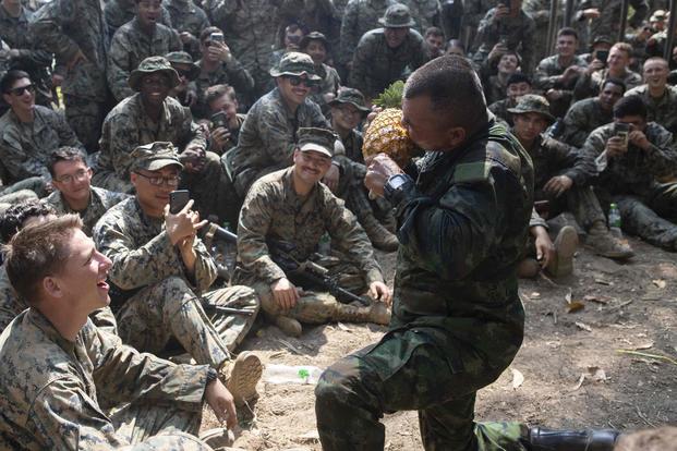 U.S. Marines observe as a Royal Thai Marine instructor eats a pineapple as part of jungle survival training.