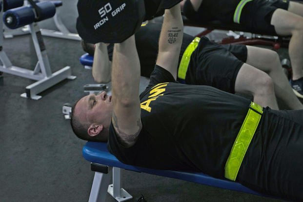 A staff sergeant performs a bench press with dumbbells.