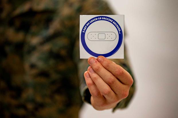 A U.S. Marine holds out a sticker after receiving the COVID-19 vaccination