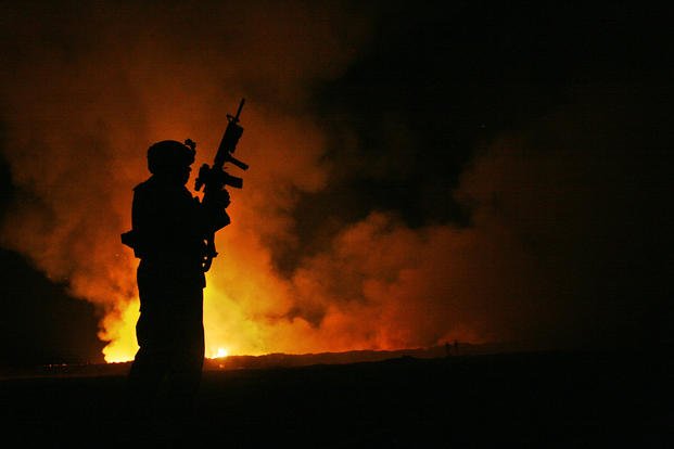 Sgt. Robert B. Brown, with Regimental Combat Team 6, Combat Camera Unit watches over the civilian firefighters at the burn pit as smoke and flames rise into the night sky behind him.