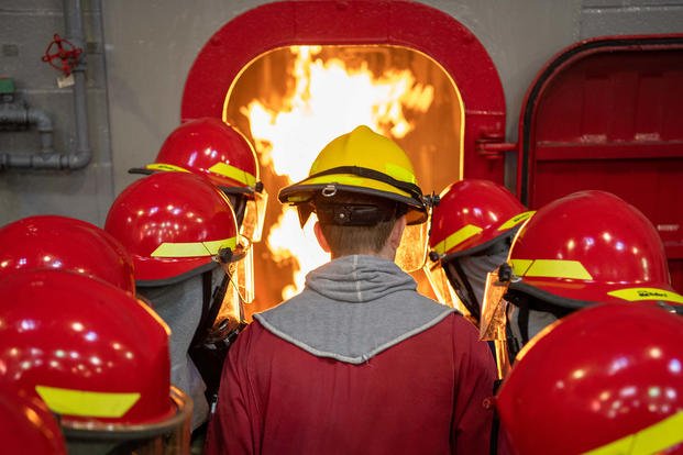 Recruits spray a hose into a simulated fire during a firefighting training exercise inside the USS Chief Fire Fighter Trainer at Recruit Training Command. 