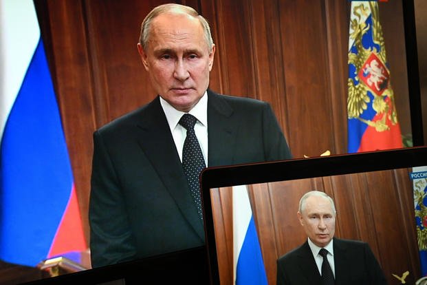 Russian President Vladimir Putin is seen on monitors as he addresses the nation
