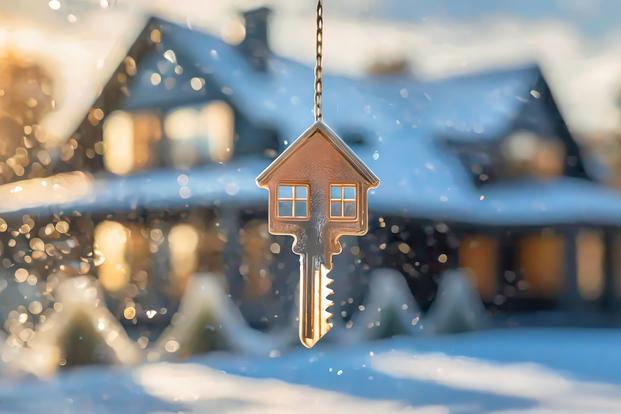 A key shaped like a house dangles in the foreground of a sparkly image of a snow-dusted, garland-wrapped house