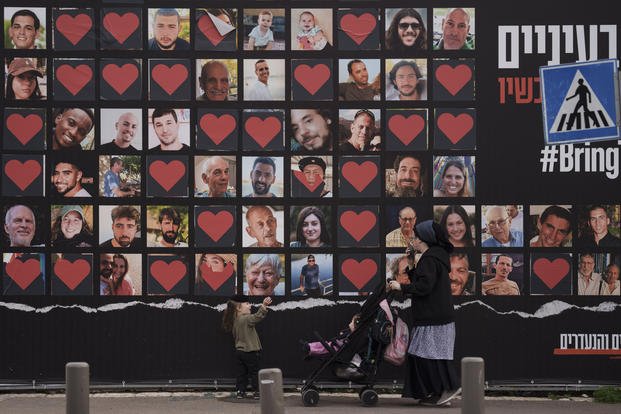 A woman and her children walk past a wall with photographs.