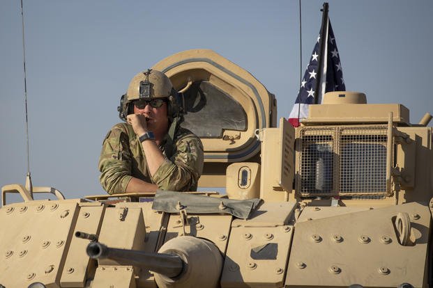 A U.S. soldier in Syria observes form the top of a fighting vehicle