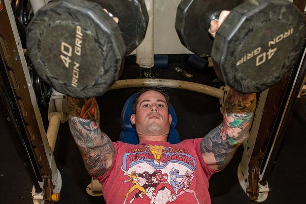 Culinary Specialist 1st Class Bennett Evans uses dumbbells for the bench press during a physical training session aboard Arleigh Burke-class guided-missile destroyer USS Dewey (DDG 105) in the East China Sea. 