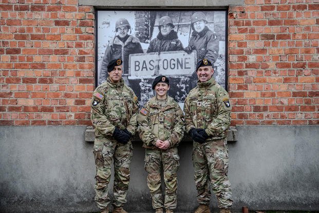 Three modern-day 101st Airborne troops now in Bastogne in front of a photo of 101st leaders who defended the town in December 1944.