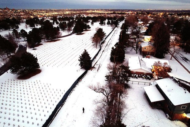 Henry Navarro stands between the long black fence at the edge of Fort Logan National Cemetery