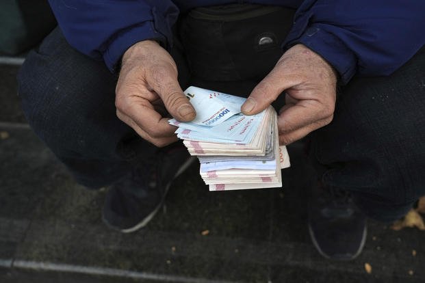 A street money exchanger poses for a photo without showing his face as he counts Iranian banknotes