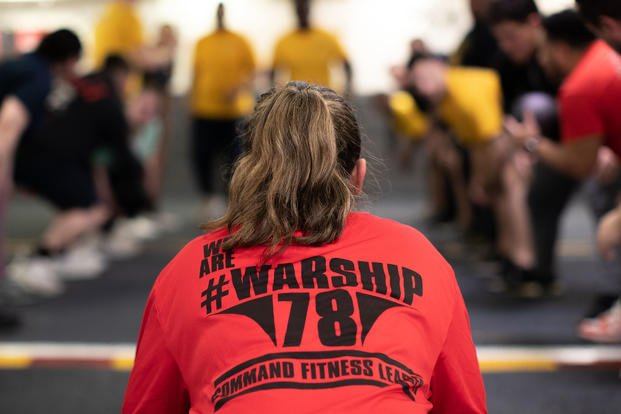 A retail services specialist 3rd class, assigned to the USS Gerald R. Ford’s (CVN 78) supply department, conducts a command fitness class in the hangar bay.