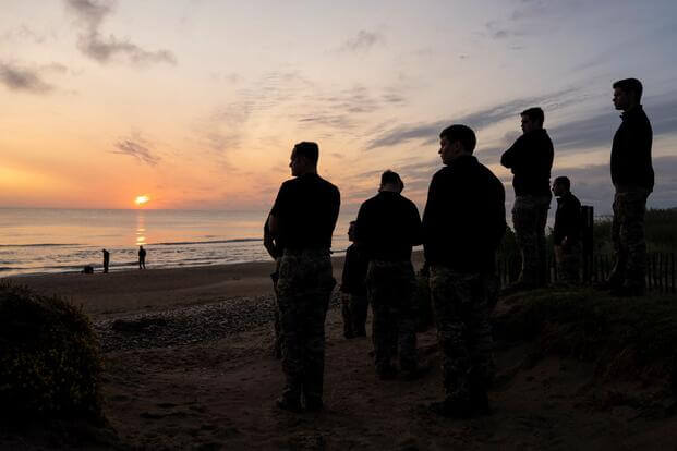 Men silhouetted watch the sunrise on Omaha Beach.
