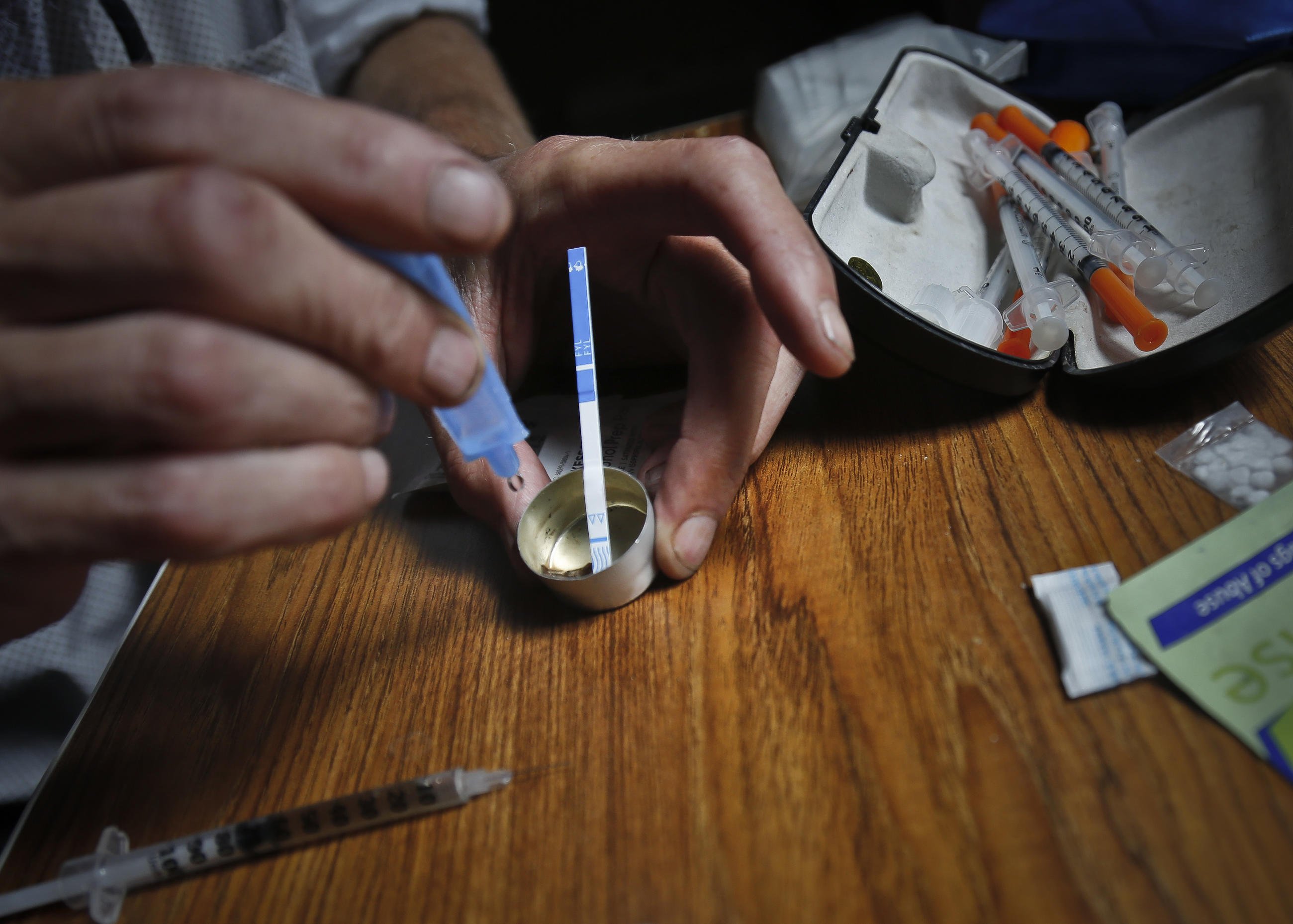 A drug user prepares heroin, placing a fentanyl test strip into the mixing container to check for contamination
