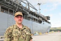 Navy Petty Officer 2nd Class Andrew Pluss, an electrician’s mate assigned to the Guam-based submarine tender USS Frank Cable, stands in front of the ship at Naval Base Guam, July 18, 2018. Pluss helped the victim of an auto-pedestrian crash in Guam July 16. (U.S. Navy photo/Alana Chargualaf)