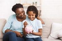 Mother watching daughter put coins into piggy bank
