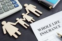 An assortment of desk items, a form labeled "whole life insurance" and wood cutouts representing a family appear on a desk
