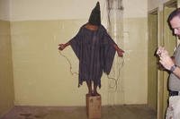 detainee standing on a box with a bag on his head and wires attached to him in the Abu Ghraib prison