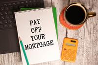 The words &quot;pay off your mortgage&quot; appear on a notebook resting on the wood top of a desk near office supplies and coffee.