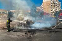 Firefighters extinguish a burning car in the courtyard of an apartment building after a missile attack.