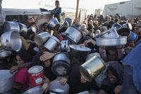 Palestinian women and girls struggle to reach for food at a distribution center in Khan Younis