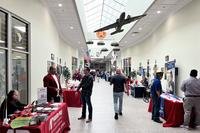 In an atrium with model airplanes and paratroopers hanging from a long skylight, military retirees talk to people at tables.
