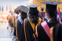 Pictured from behind, graduates with various regalia stand in a line.