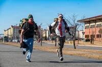 Two service members jog with backpacks of toys.
