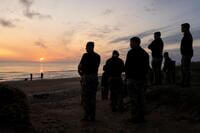 Men silhouetted watch the sunrise on Omaha Beach.