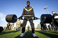 A soldier in an Army tracksuit does a deadlift outside.