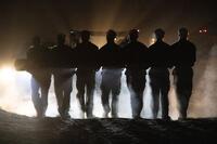 At night in silhouette, SEAL candidates carry a log together.