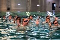 Marines tread water in a pool with their hands raised.