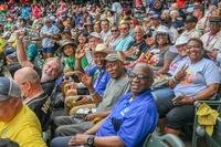 A large crowd of veterans in the stands of a sports stadium look at the camera and happily wave.