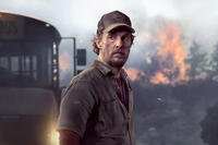 Matthew McConaughey stands near a school bus with flames rising behind him during a wildfire evacuation in The Lost Bus. Photo credit: Apple TV+