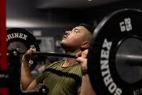 A Marine does an overhead lift with a barbell in a gym.