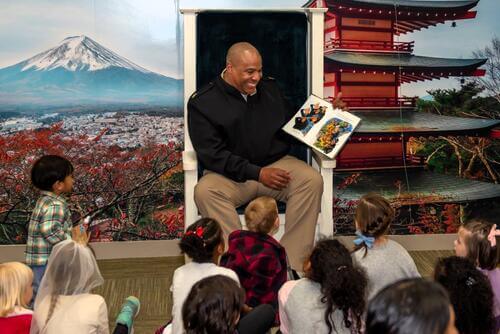 A senior member of the Navy reads a book to kids at storytime.
